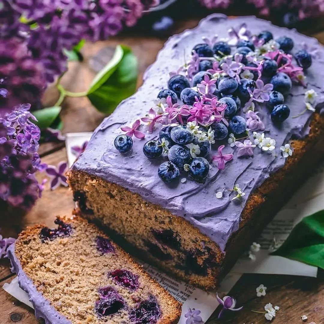 Blueberry cake with purple frosting topped with fresh berries and lilac flowers.