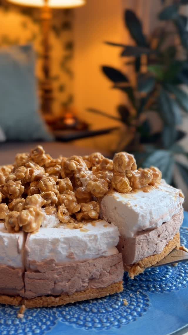 Layered chocolate and cream cake topped with golden caramel popcorn on a blue plate.