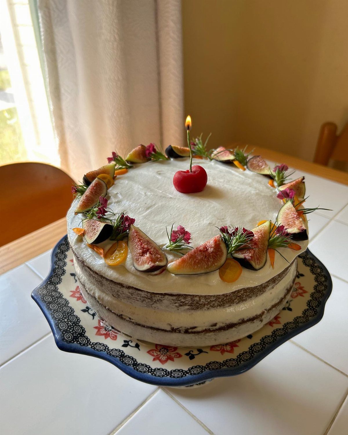 Layered cake topped with fresh figs, orange slices, and a lit cherry candle.