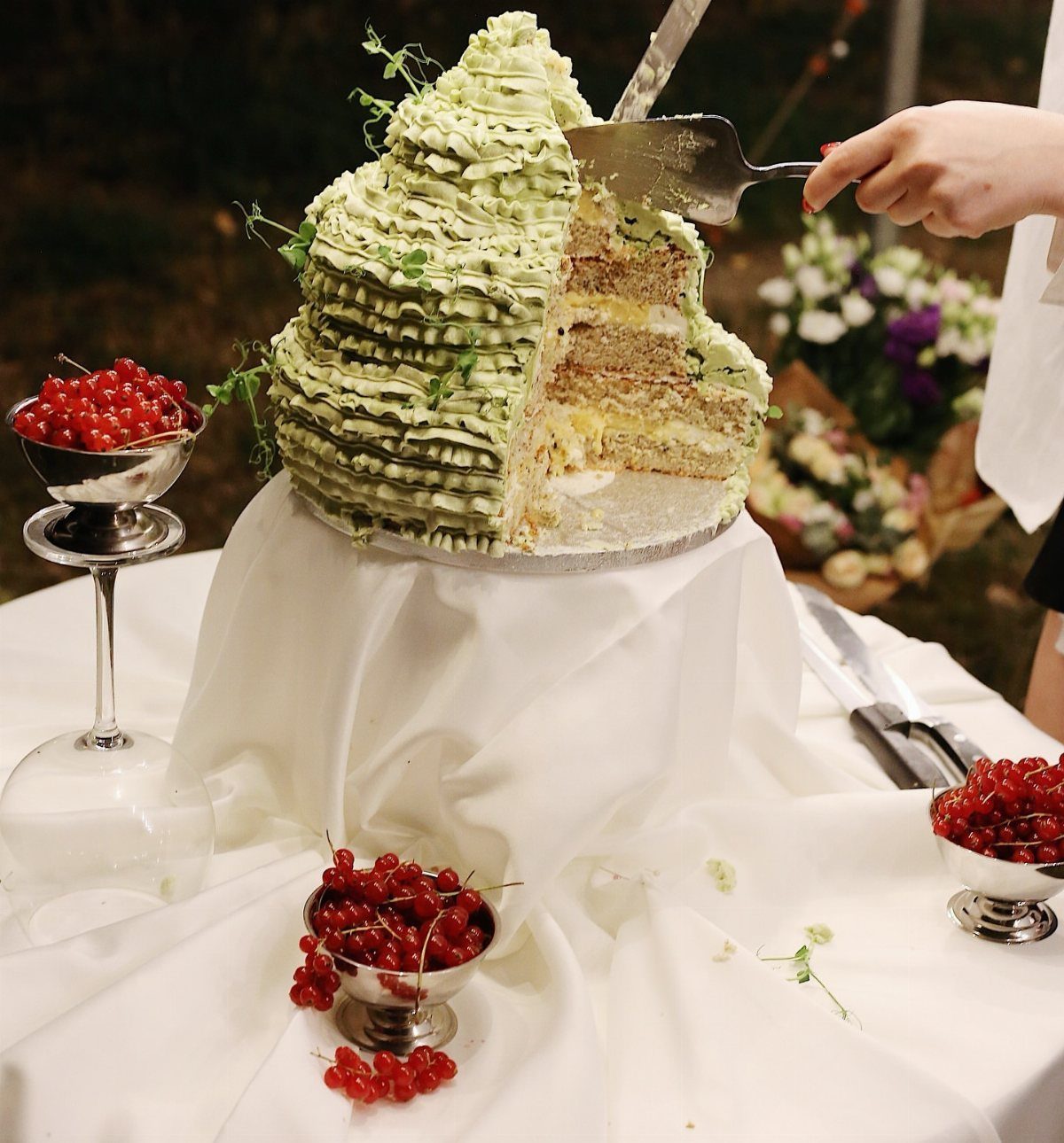 Multi-layered cake with pale green ruffled frosting and red currants on white table