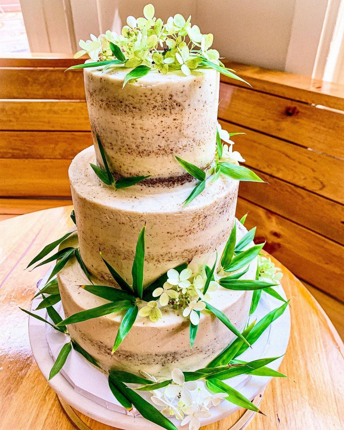 Three-tier naked vanilla cake decorated with green leaves and small white flowers.
