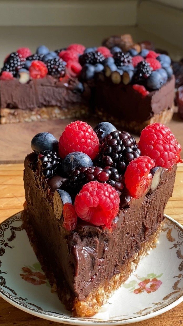 Chocolate cake slice topped with fresh raspberries, blueberries, and blackberries on a floral plate.