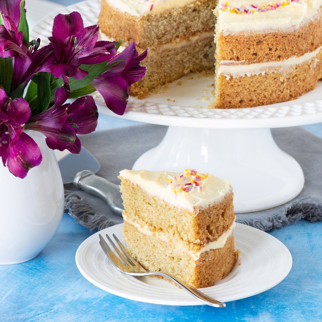 Two-layer white cake with sprinkles on a stand and a slice on a plate.