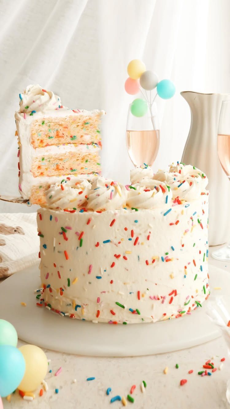 White frosted layer cake with colorful sprinkles and a slice removed.