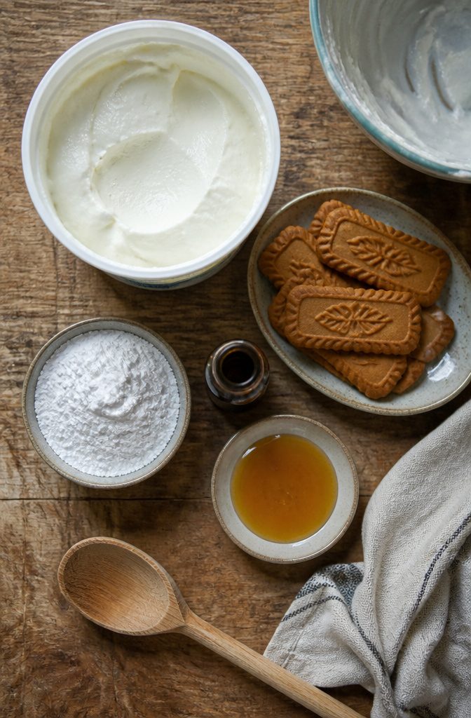 Greek yogurt tub beside Biscoff cookies with sugar and vanilla nearby