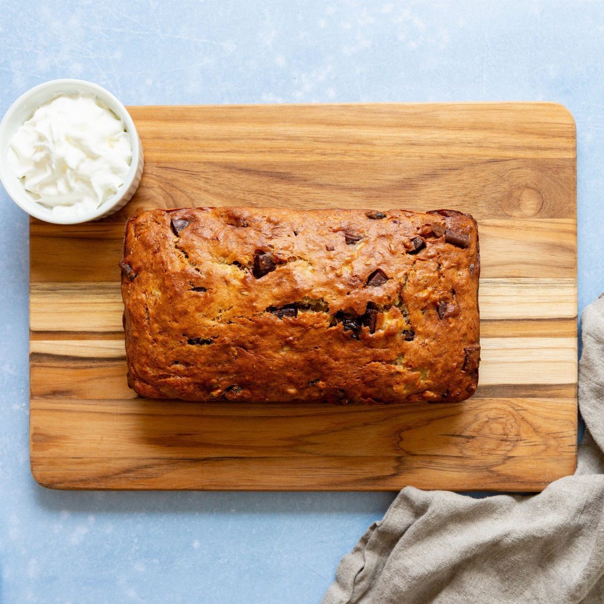 32 Ideas on What to Serve for Breakfast, From Eggs to Scones 11 Banana bread loaf on a wooden board with a side of white cream.