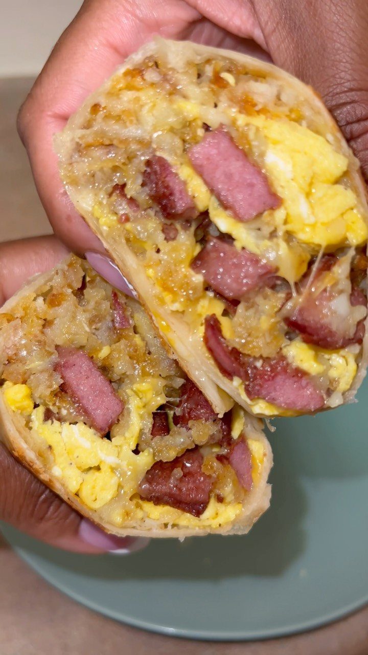 32 Ideas on What to Serve for Breakfast, From Eggs to Scones 7 Sliced breakfast burrito filled with eggs, sausage, and potatoes held in two hands.