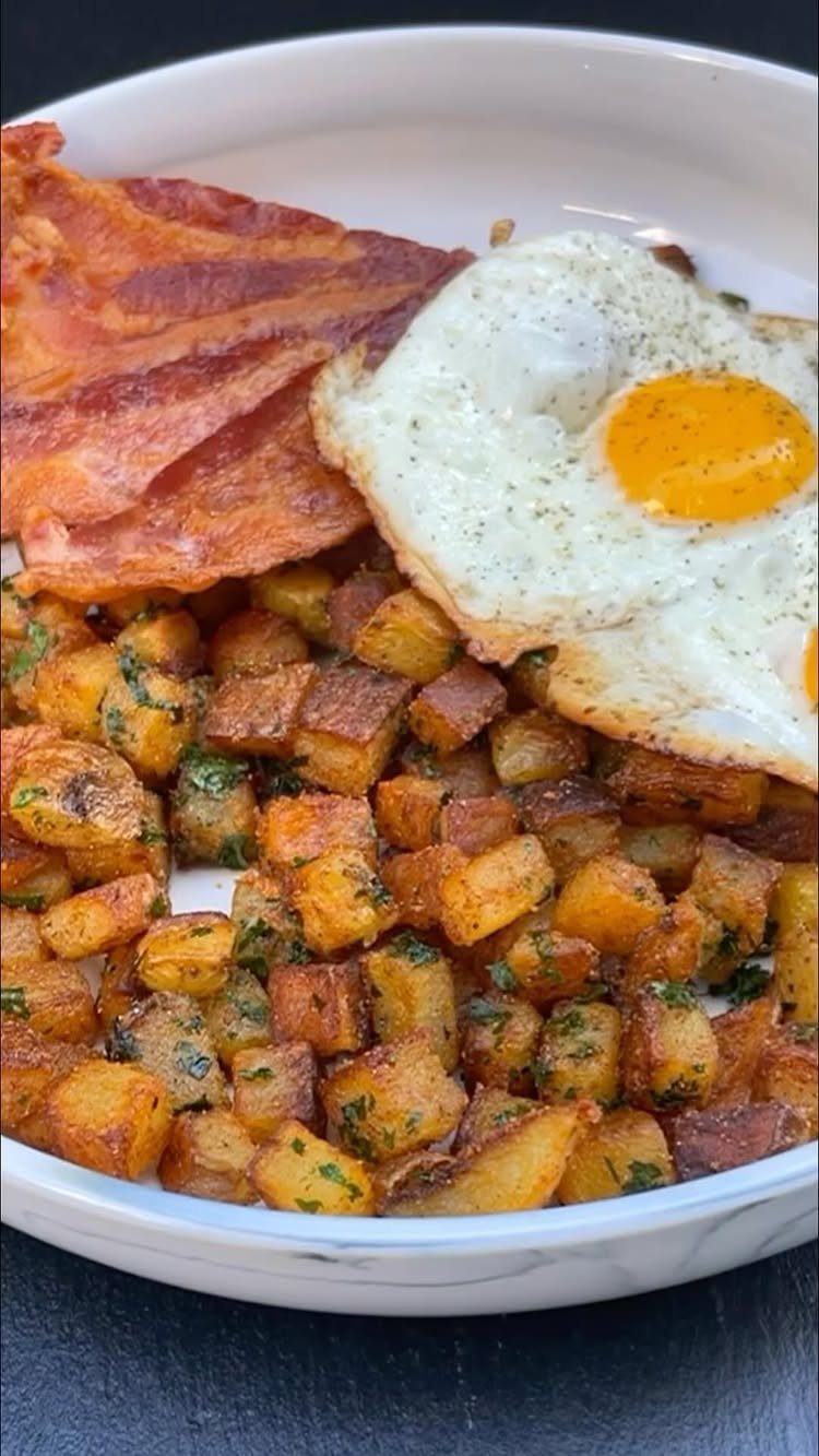 32 Ideas on What to Serve for Breakfast, From Eggs to Scones 22 Cubed breakfast potatoes with a fried egg and crispy bacon in a white bowl.