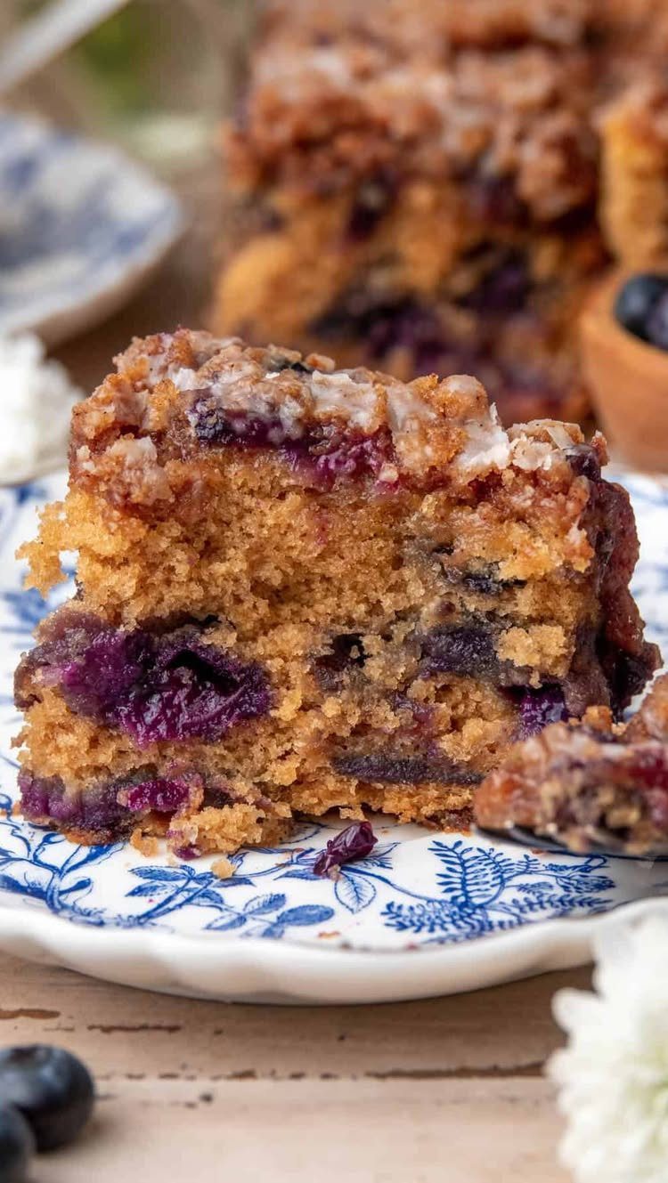 32 Ideas on What to Serve for Breakfast, From Eggs to Scones 13 Blueberry coffee cake slice with streusel topping on a blue and white patterned plate.