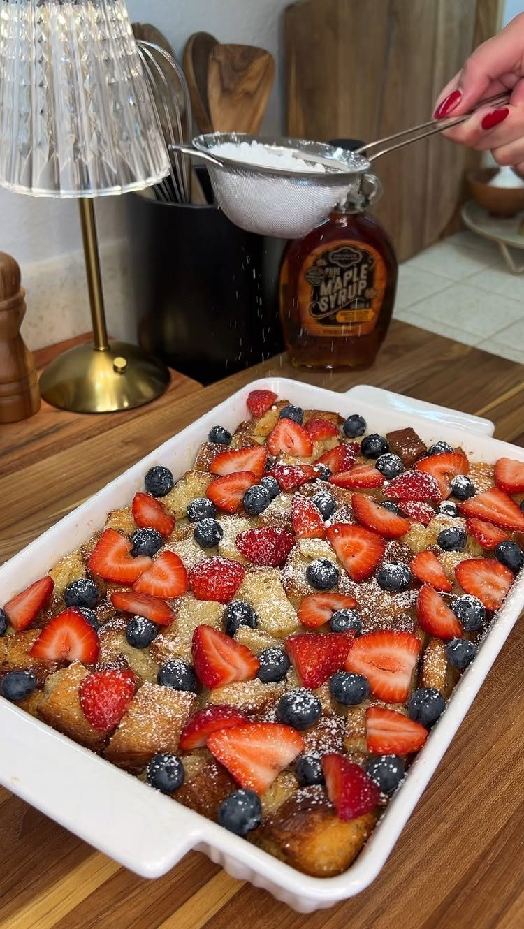 32 Ideas on What to Serve for Breakfast, From Eggs to Scones 2 French toast casserole with strawberries and blueberries being dusted with powdered sugar.