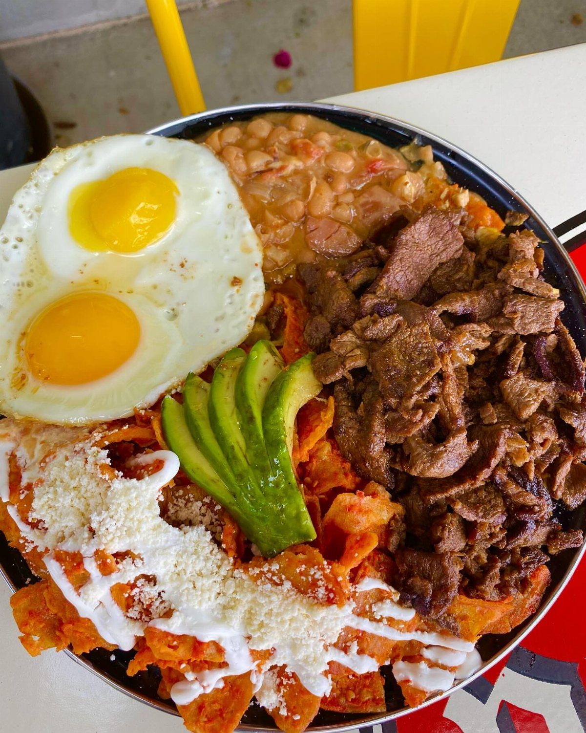 32 Ideas on What to Serve for Breakfast, From Eggs to Scones 31 Huevos rancheros with fried eggs, avocado, meat, beans, and chips on a metal plate.