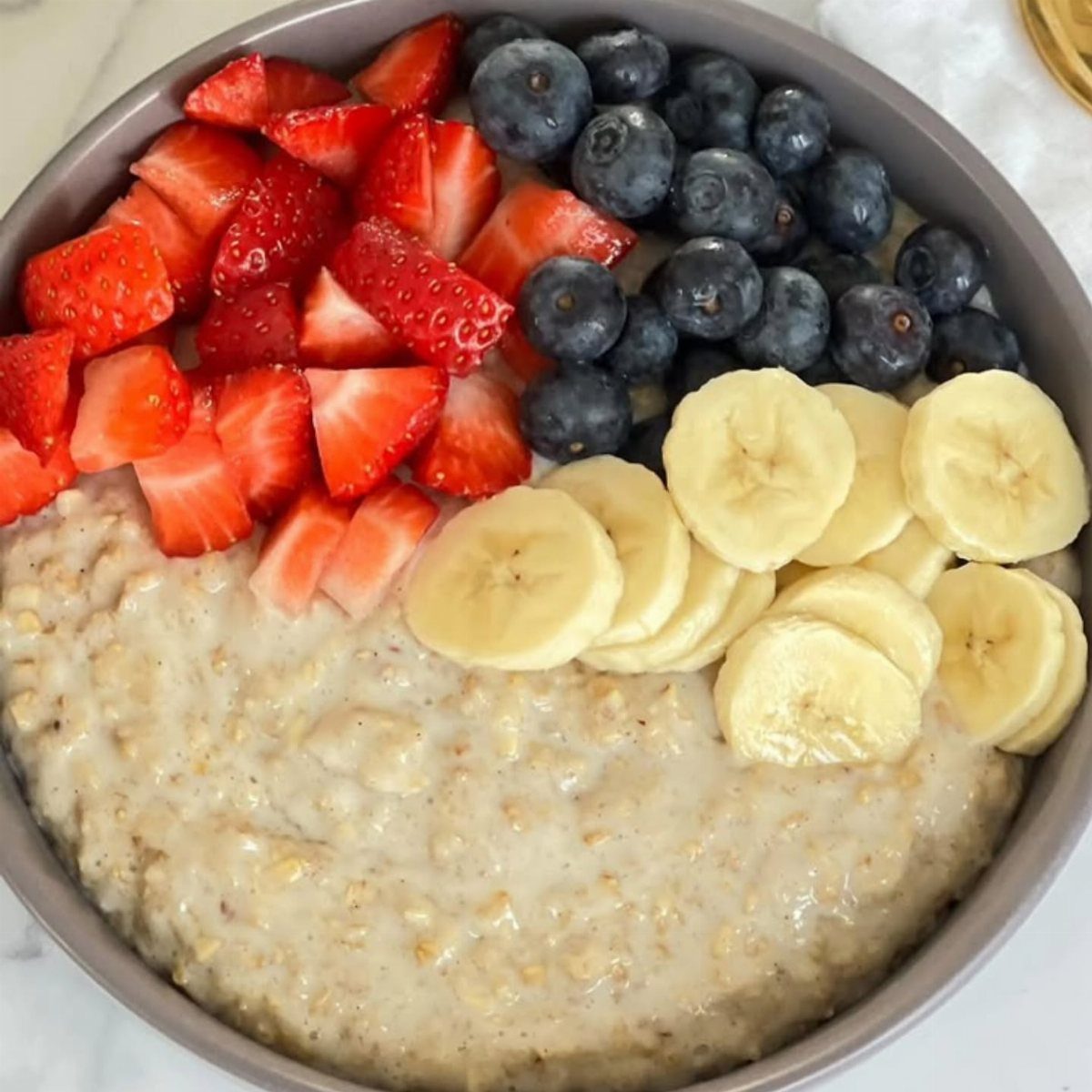 32 Ideas on What to Serve for Breakfast, From Eggs to Scones 12 Oatmeal in a grey bowl topped with strawberries, blueberries, and sliced bananas.